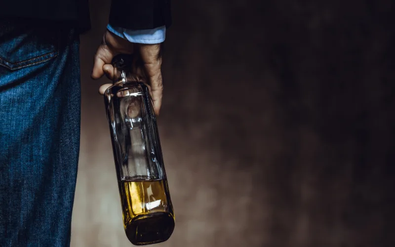 Man holding a half-empty bottle of liquor at his side